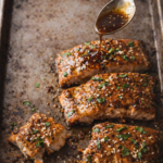 Teriyaki glazed salmon fillets on a well used baking sheet with sauce being spooned over the top