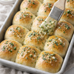 Soft homemade garlic butter dinner rolls on a baking sheet being brushed with melted garlic butter glaze.