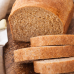 Soft homemade whole wheat bread loaf sliced on a wooden cutting board with golden crust and fluffy interior