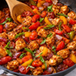 Honey balsamic chicken and peppers cooking in a skillet with bell peppers and onions coated in a glossy balsamic sauce.