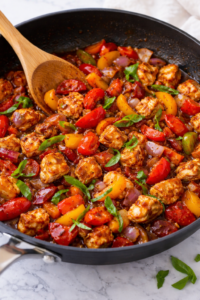 Honey balsamic chicken and peppers cooking in a skillet with bell peppers and onions coated in a glossy balsamic sauce.