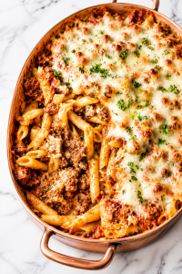 Easy meaty baked ziti in a copper baking dish with melted cheese and rich meat sauce on a white marble countertop
