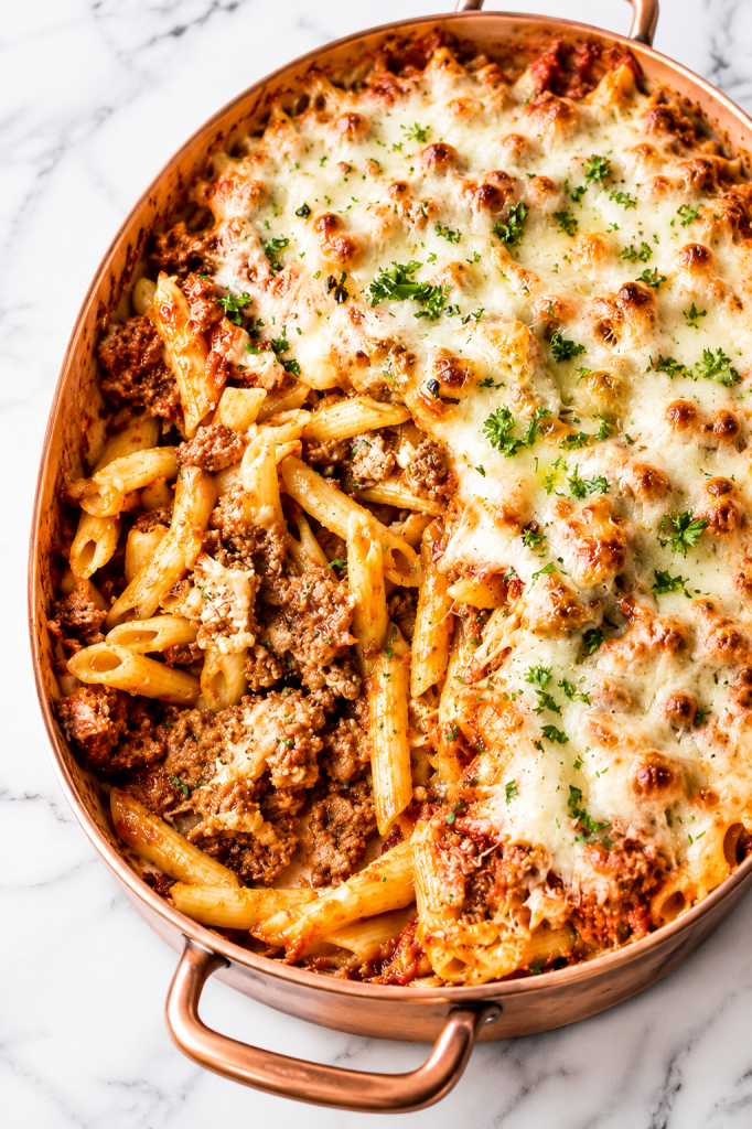 Easy meaty baked ziti in a copper baking dish with melted cheese and rich meat sauce on a white marble countertop