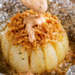 Viral onion boil baked in foil topped with crispy fried onions and drizzled with creamy bloom sauce
