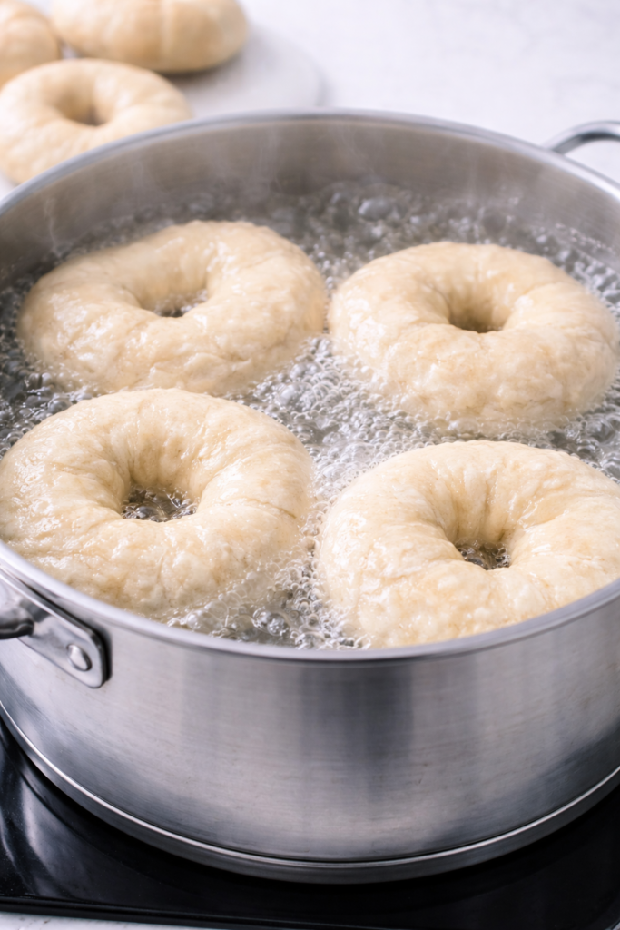 Homemade bagels boiling in a pot of water before baking, showing the traditional step that creates a chewy bagel texture.