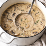 Copycat Sweet Tomatoes cream of mushroom soup in a white enamel pot with a silver ladle.