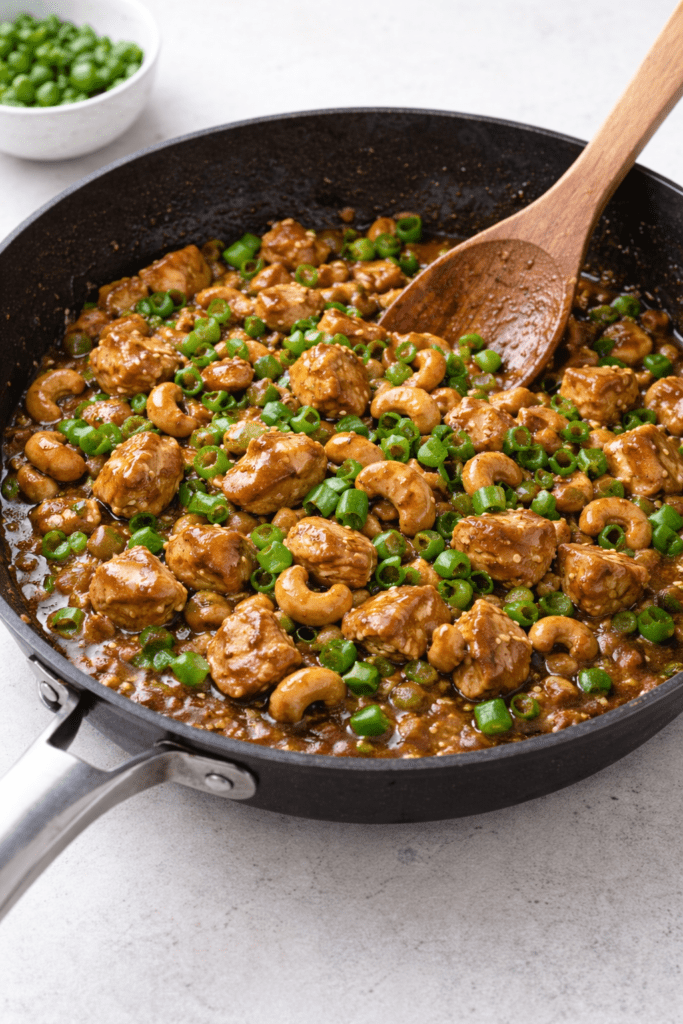 Easy chicken with cashews cooking in a skillet with green onions and glossy savory sauce