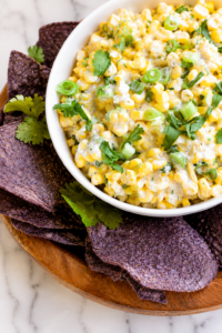 Close-up of creamy spicy ranch corn salsa topped with green onions and cilantro served with blue corn tortilla chips.