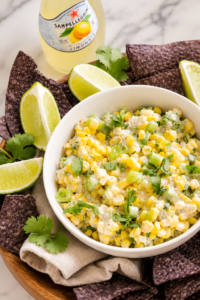 Creamy spicy ranch corn salsa in a white bowl with blue corn tortilla chips and fresh lime wedges on a marble countertop.