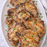 Grilled maple Dijon pork chops arranged on a large white platter with fresh herbs.