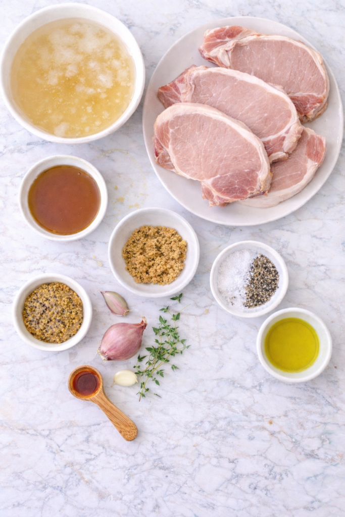 Flat lay of ingredients for grilled maple Dijon pork chops on a white marble background.