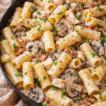 Creamy bacon mushroom chicken pasta with rigatoni in a skillet, rich garlic cream sauce and fresh herbs, cozy weeknight dinner.