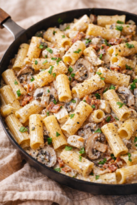 Creamy bacon mushroom chicken pasta with rigatoni in a skillet, rich garlic cream sauce and fresh herbs, cozy weeknight dinner.