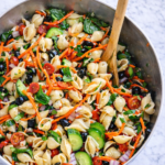 Deli style pasta salad in a large bowl with shells, vegetables, and Italian dressing on a marble countertop