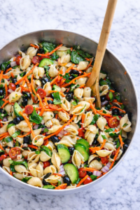 Deli style pasta salad in a large bowl with shells, vegetables, and Italian dressing on a marble countertop