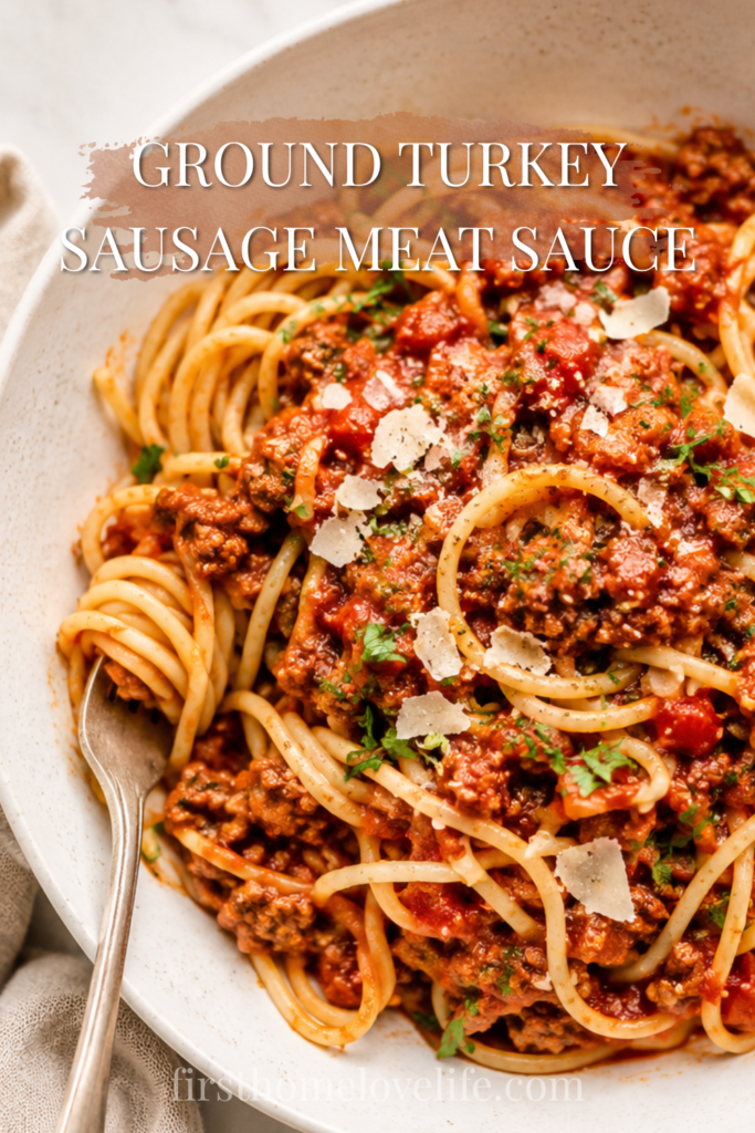 Large bowl of spaghetti topped with hearty ground turkey and sausage meat sauce, garnished with Parmesan cheese and fresh herbs on a marble countertop.