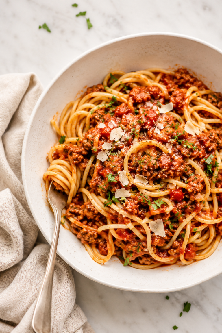 Large white bowl of spaghetti topped with hearty ground turkey and sausage meat sauce on a white marble countertop with a neutral linen cloth.