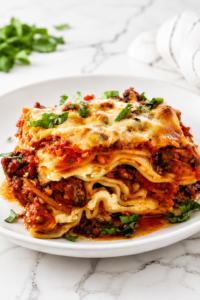 A thick slice of homemade meat lovers lasagna layered with ground beef, Italian sausage, ricotta cheese, mozzarella, and rich tomato sauce on a white plate atop a white marble countertop.