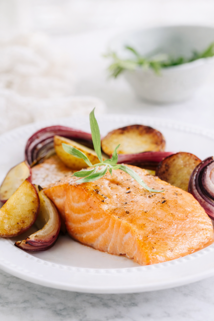 Sheet pan roasted salmon with baby potatoes and red onions on a white plate over a marble countertop.