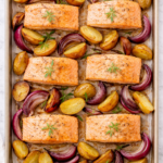 Overhead view of sheet pan salmon with roasted baby potatoes and red onions on parchment-lined baking sheet.