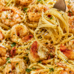 Fork twirling linguine topped with garlic butter shrimp scampi on a large white platter with fresh parsley, Parmesan, lemon, and red pepper flakes.