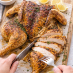 Slicing lemon thyme spatchcock chicken on a cutting board with crispy golden skin