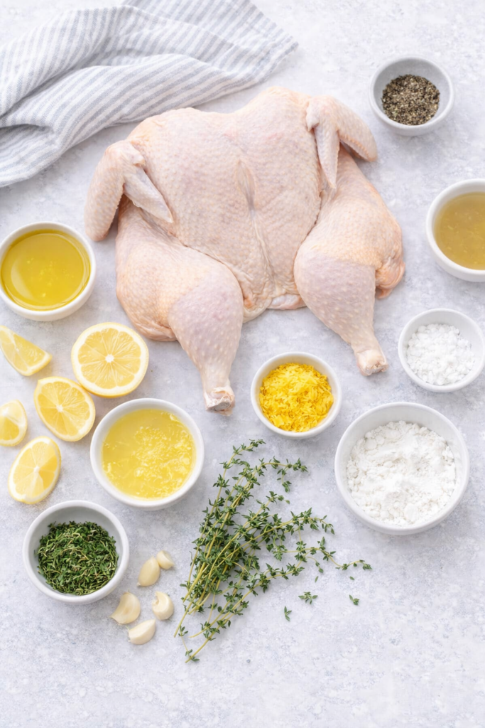 Flat lay of lemon thyme spatchcock chicken ingredients on a light marble background