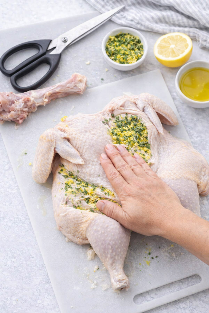 Spatchcock chicken being prepped with lemon thyme herb mixture under the skin