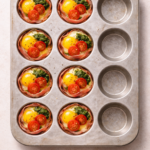 Prosciutto-wrapped baked eggs in a muffin tin with pesto and cherry tomatoes