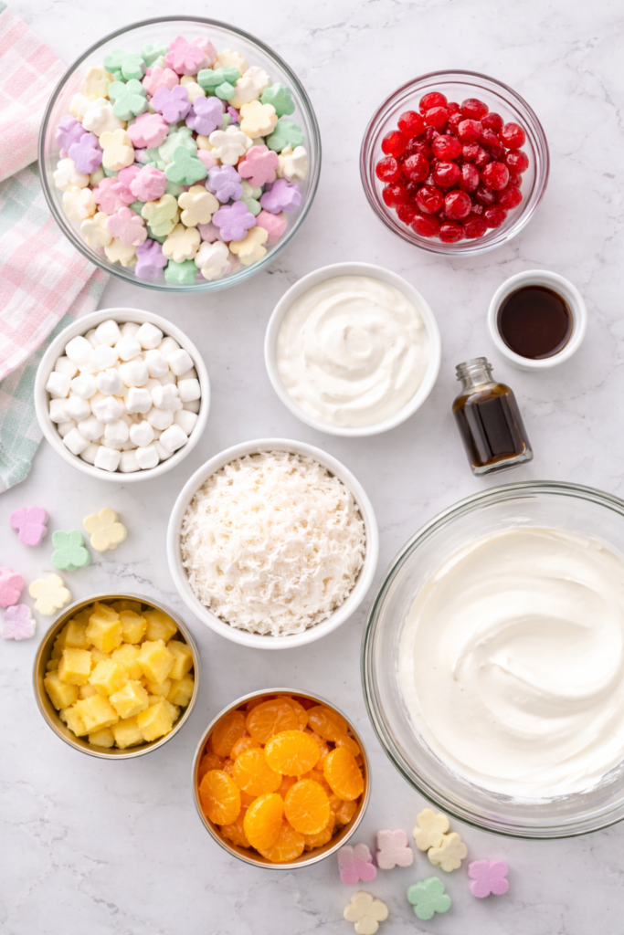 Flat lay of Easter ambrosia salad ingredients including bunny marshmallows, mandarin oranges, pineapple, cherries, coconut, and whipped cream