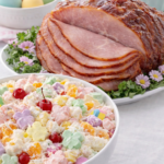 Creamy Easter ambrosia salad with pastel bunny marshmallows served next to sliced glazed ham on a spring Easter brunch table