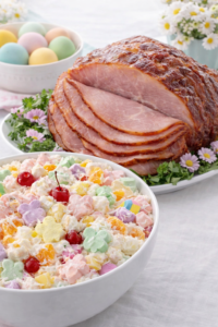 Creamy Easter ambrosia salad with pastel bunny marshmallows served next to sliced glazed ham on a spring Easter brunch table