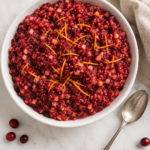 Fresh cranberry relish with orange and apple served in a white bowl and garnished with orange zest.