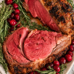 herb butter prime rib roast sliced on platter with rosemary and cranberries