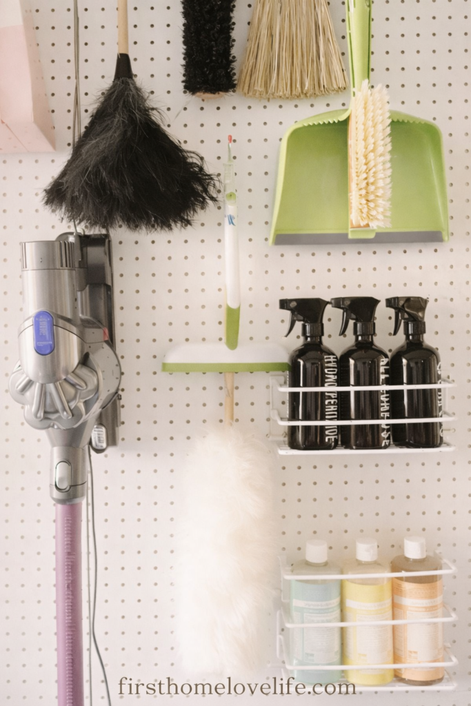 cleaning command center pegboard with organized spray bottles, dusters, broom and vacuum storage