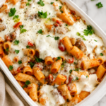 Cheesy baked rigatoni and Italian sausage casserole in a white baking dish on a marble countertop with a neutral linen towel.