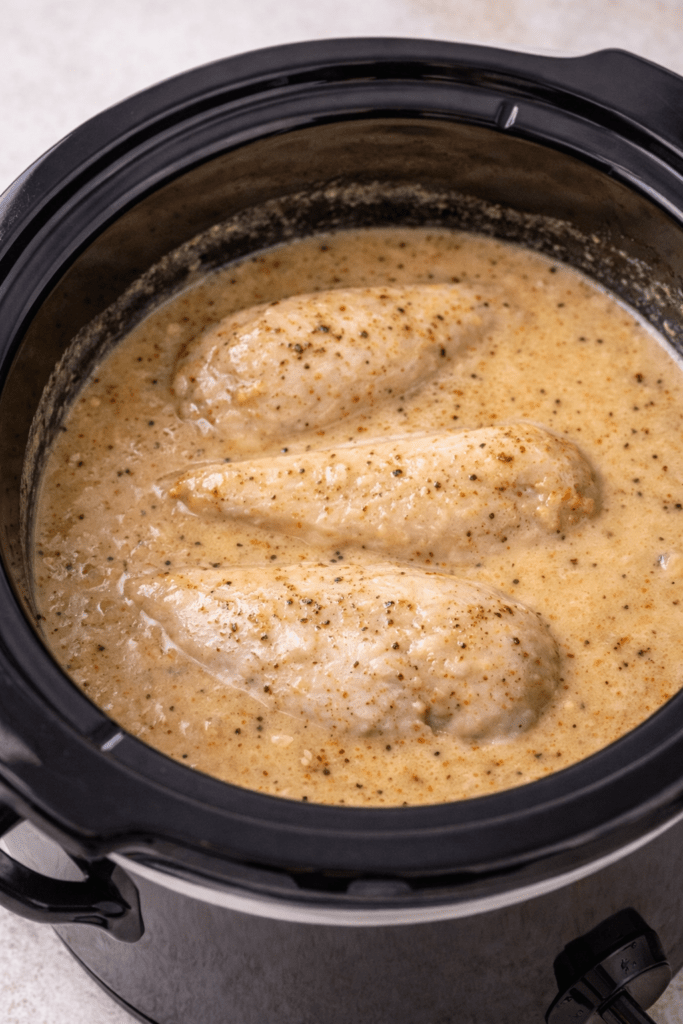 Chicken breasts cooking in creamy gravy inside a slow cooker