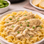 Slow cooker chicken breast with creamy gravy served over egg noodles with crockpot in background