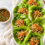 Thai chicken lettuce wraps served on a white oval platter with crisp butter lettuce, savory ground chicken filling, and a homemade Thai dipping sauce on a marble countertop.