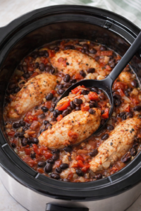 Southwestern chicken with black beans cooking in a slow cooker with roasted red peppers and tomatoes