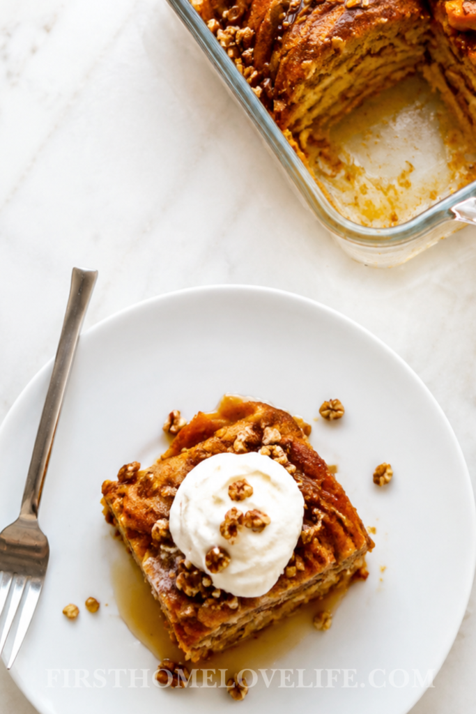 Plated serving of cinnamon pumpkin pancake cake topped with whipped cream, maple syrup, and pecans beside the baking dish