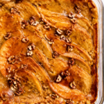 Overhead view of cinnamon pumpkin pancake cake baked in a clear glass dish with maple syrup and chopped pecans