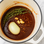 Homemade BBQ sauce simmering in a Dutch oven with onion, garlic, fresh thyme, and red pepper flakes.