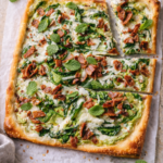 Spring pea and bacon flatbread with creamy pea mint sauce, melted Gruyère cheese, crispy bacon, and fresh mint on a golden rectangular crust.
