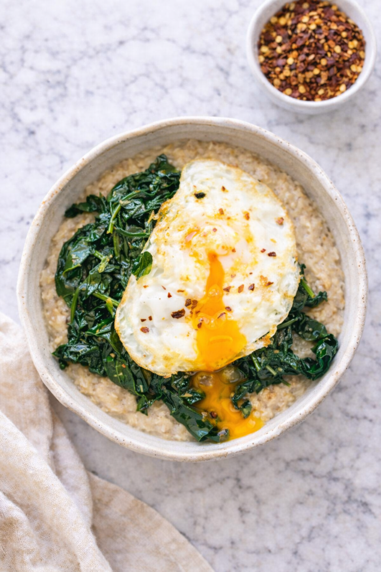 Savory oatmeal topped with sautéed spinach and a runny fried egg in a rustic pottery bowl on a marble countertop