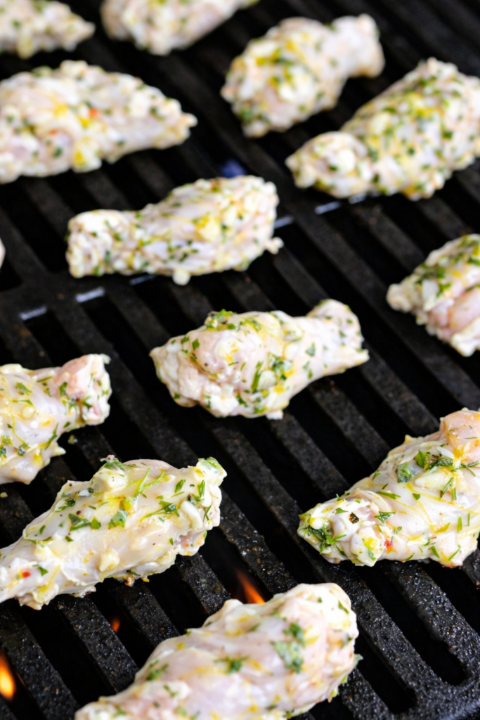 Marinated Greek style chicken wings grilling on black grill grates with lemon, garlic, and herb marinade visible