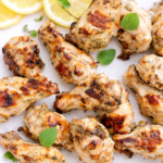 Greek style grilled chicken wings on a white plate with lemon slices and fresh oregano leaves