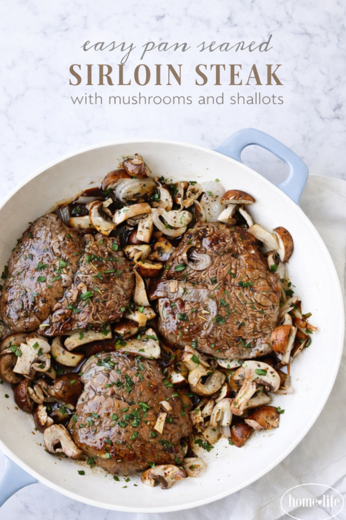 Easy pan-seared sirloin steak cooked in a white skillet with sautéed mushrooms and shallots on a light marble background.