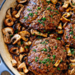 Pan-seared sirloin steak simmered in a rich sauce with sautéed mushrooms and shallots in a white skillet, garnished with fresh parsley.