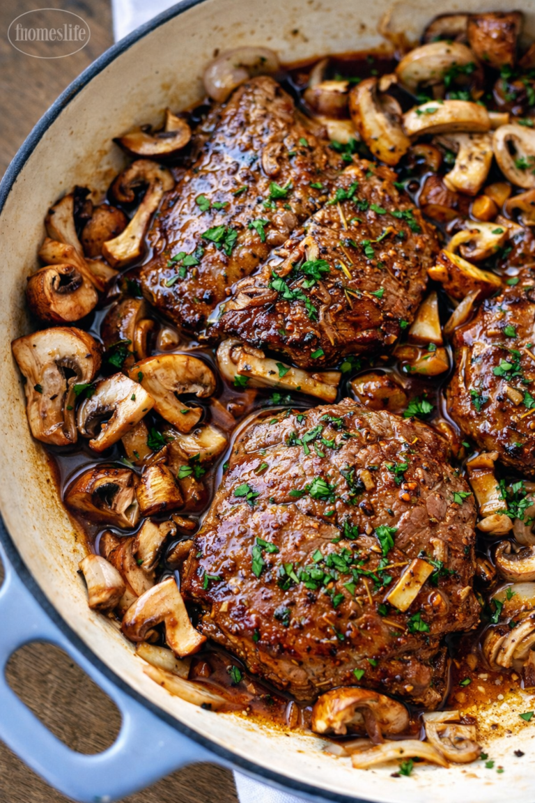 Pan-seared sirloin steak simmered in a rich sauce with sautéed mushrooms and shallots in a white skillet, garnished with fresh parsley.